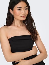 Musta olkaimeton toppi, jossa sileä ja joustava kangas. Pitkät tummat hiukset, joissa hennot laineet. Luonnollinen meikki ja hopeiset korvakorut korostavat ilmettä.