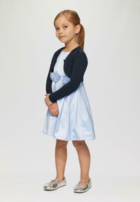 Helles blaues Satin-Kleid mit tailliertem Oberteil und ausgestellt Rock, akzentuiert durch eine dunkelblaue Strickjacke und silberne Schuhe. Rosenverzierungen an der Taille.