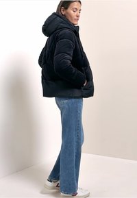Doudoune noire avec un design matelassé et une capuche, associée à un jean flare bleu clair et à des baskets blanches avec des accents rouges.