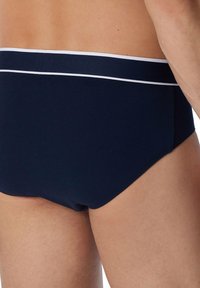 Slip da nuoto blu navy con una banda bianca decorativa, caratterizzati da una texture liscia e da un design aderente che si adatta al corpo.