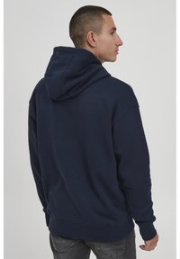 Navyblauer Hoodie mit lockerer Passform, großer Kapuze und gerippten Bündchen und Saum. Glatte Textur, minimalistische Details.