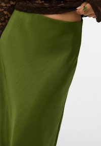 Groene rok tot op de knie van gladde stof, met een zijdrapering, een lichte glans en een eenvoudige textuur.