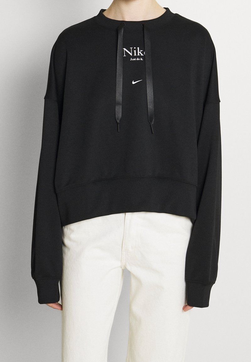 Svart kort tröja med långa ärmar, med en vit Nike-logotyp och texten "Just do it.", dragsko i huvan och slät tygstruktur.