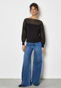 Czarna sweater z koronkowymi detalami na ramionach i rękawami w stylu balonowym, w połączeniu z dżinsami w szerokim kroju w kolorze niebieskim i czarnymi butami.