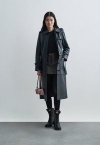 Melnas ādas trenčs, tumša svārki, melnas legingi, kažokādas oderēti melni zābaki ar zelta akcentiem un neliela rozā rokassoma. Minimalistisks dizains.