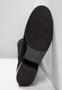 Semelle de botte en daim noir avec finition lisse, comportant des logos et motifs embossés, talon plat et traction en caoutchouc pour l'adhérence.