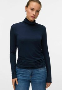 Marineblå langærmet turtleneck top lavet af glat, strækbart stof, tætsiddende design, diskret samlet ved taljen, parret med blå jeans.