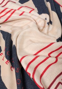 Sciarpa multicolore realizzata in morbido tessuto, caratterizzata da un design astratto con elementi blu, beige e rossi; texture liscia e aspetto drappeggiato.