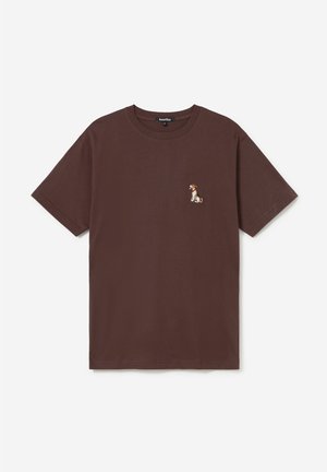 T-shirt marron à manches courtes avec un petit chien assis brodé sur le côté gauche de la poitrine et un col rond.