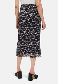 Jupe noire mi-longue avec un motif abstrait blanc, ourlet festonné et superposition transparente, associée à des chaussures à talons blocs noires.