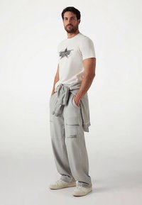 White t-shirt with a black star logo, paired with loose gray pants featuring pockets and text accents, worn with white sneakers.