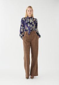 Pantaloni a quadri lunghi e marroni con vestibilità ampia, abbinati a una blusa blu floreale con fiocco. Tessuto morbido, con modelli floreali sottili.