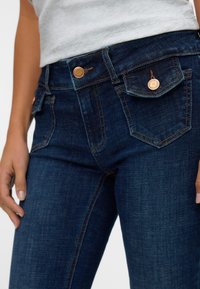 Dark denim jeans featuring a high waist, copper rivet accents, two front pockets, and a smooth texture with contrasting orange stitching.