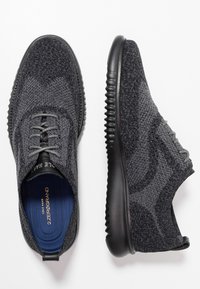 Scarpe sportive nere con tomaia in maglia testurizzata e suole in gomma. Presentano lacci grigi e un'intersuola ammortizzata con il marchio "2.ZEROGRAND".