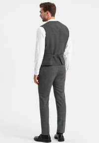 Grijze colbert met een getailleerd ontwerp en subtiele textuur, gecombineerd met bijpassende grijze broek en zwarte schoenen. Witte shirt eronder.
