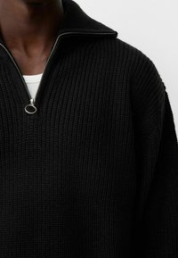 Svart stickad tröja med hög krage och halv dragkedja. Texturerad tyg med ribbat mönster. Utrustad med silverdetaljer på dragkedjan.