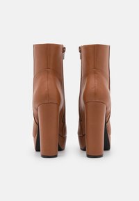 Paire de bottines en cuir marron avec talons carrés, vue arrière sur fond blanc.