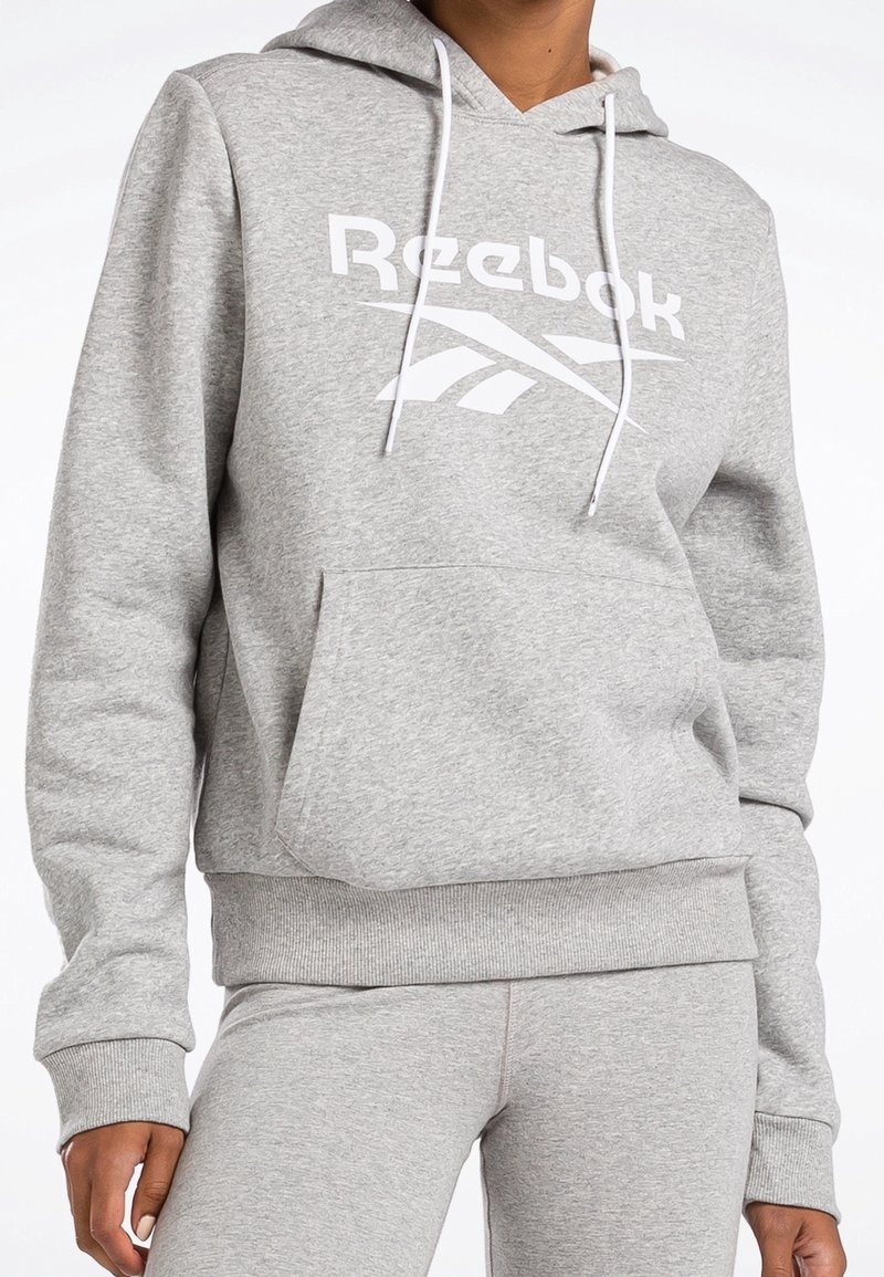 Felpa grigia con cappuccio regolabile, vestibilità oversized, tasca a marsupio e grande logo Reebok bianco sul davanti. Tessuto morbido e strutturato.