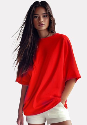 T-shirt rosso oversize con maniche corte, texture liscia e vestibilità ampia. Indossato con pantaloni corti bianchi, su uno sfondo neutro.