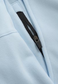 Heller blauer Stoff mit glatter Textur verfügt über einen schwarzen Reißverschluss entlang der Naht, der funktionale Details zum Design beiträgt.