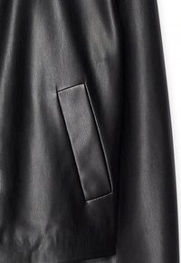 Tissu en cuir noir lisse avec une poche rectangulaire cousue sur le côté droit, montrant un léger éclat et une texture.