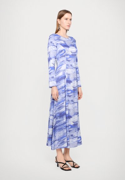 Long-sleeve dress in shades of blue with abstract patterns, fitted bodice, flowing skirt, and black heeled sandals. Smooth fabric texture.
