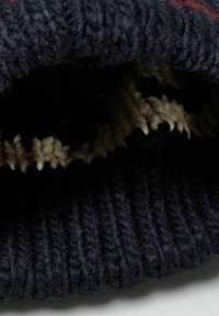 Gros plan sur un tissu tricoté noir avec une texture côtelée et un aperçu d'un tricot à motif noir et blanc à l'intérieur.