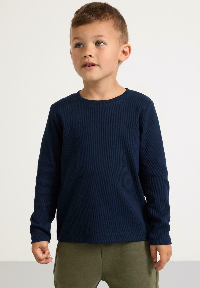 Marinblå långärmad t-shirt i bomull med ribbad struktur, rund halsringning och bekväm passform, i kombination med olivgröna byxor.