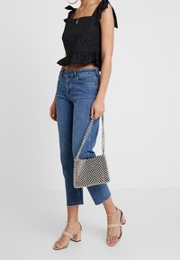 Svart croppad topp med volangkant och knytband, matchad med blå raka jeans, beige klacksandaler med blockheel och en silverfärgad spikad väska.