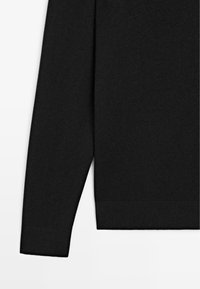 Schwarzer Strickpullover mit geripptem Bündchen und Saum, lockerer Passform und glatter Textur, der einfache, minimalistische Designdetails präsentiert.