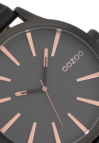 Montre analogique noire avec un cadran à motif hexagonal, index et aiguilles en rose doré, dotée d'un élégant bracelet noir. Marque : OOZOO.