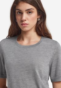 Grå kortærmet sweater med en rund halsudskæring, glat tekstur og diskret syning ved ærmerne. Ingen synlige mønstre eller grafik.