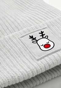 Light gray knit beanie with a ribbed texture. Features a square patch depicting a cartoon reindeer with closed eyes and a red nose.