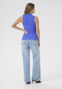 Kungablå ärmlös topp med hög krage, i kombination med ljusblå vida jeans, stylad med svarta klackskor.