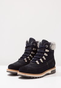 Marineblaue Wildleder-Wanderschuhe mit Kunstfellkragen, beigem Besatz, Metallösen und dicker Gummisohle. Verfügt über ein schnürbares Design für einen sicheren Sitz.