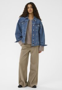 Traper jakna u srednje plavoj boji s kopčanjem na dugmad, širokim rukavima i dva prednja džepa. Uparena s bež rebrastim svijetlom džemperom i bež hlačama širokih nogavica.