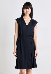 Navy blue dress with a V-neckline, short sleeves, and a cinched waist featuring a metal buckle. Smooth, lightweight fabric with minimal detailing.