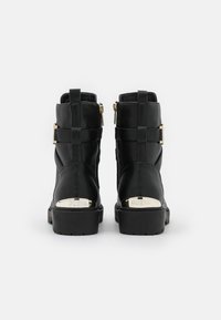 Bottines noires en cuir avec une finition texturée, accents en métal doré, et un talon bloc, présentant un détail métallique de marque à l'arrière.