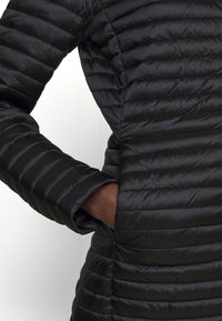 Schwarze Pufferjacke mit gestepptem Design, ausgestattet mit horizontalen Streifen, einer Innentasche und glatter, glänzender Textur.