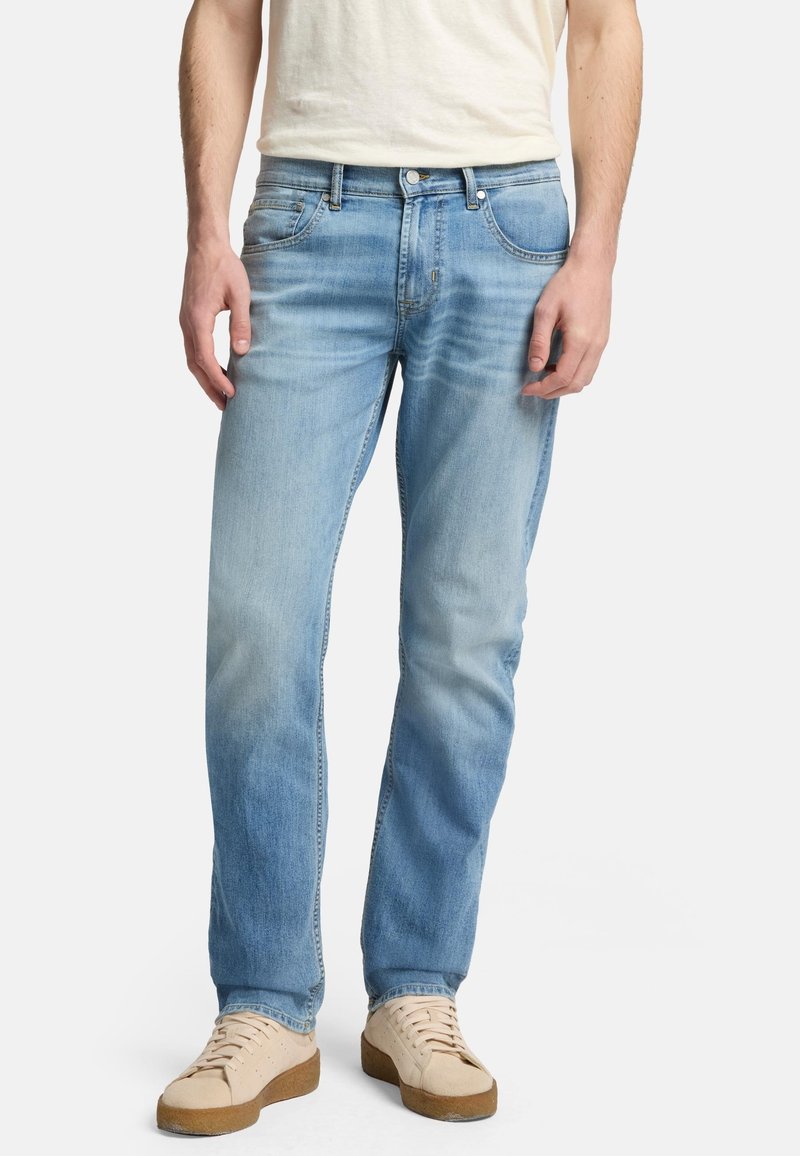 Jeans in denim azzurro chiaro con vestibilità regolare, caratterizzati da tasche anteriori e dettagli sbiaditi. Abbinati a sneakers in suede beige.