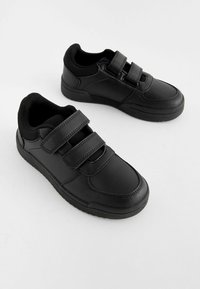 Une paire de baskets noires décontractées avec deux bandes Velcro et des cols rembourrés sur un fond blanc uni.