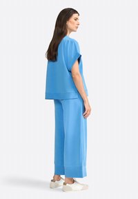 Felpa oversized azzurra chiara con maniche corte, abbinata a pantaloni larghi coordinati. Il materiale sembra morbido e liscio al tatto.