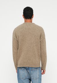 Beige neulepusero pyöreällä kaula-aukolla, raglan-hihoilla ja ribbaushelmannalla. Pehmeä rakenne, jossa on täplikkäitä kuvioita.