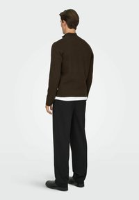 Pull en tricot marron avec un col montant, associé à un pantalon noir à jambes larges. La texture est douce et la coupe est décontractée.