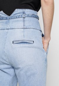 Světle modré džíny mají vysoký, v-výřezový pas, dvě boční kapsy a zadní kapsu s minimálními švy.