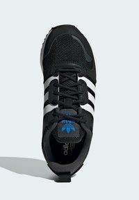 Svart idrottssko med nätöverdel och vita ränder. Har blå logotyp, runda snörningar och texturerad detaljering på sidorna.