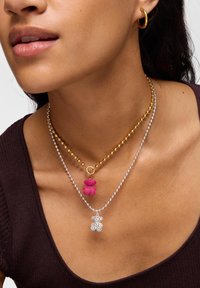 Due collane a strati: una catena d'oro con perline sferiche e un ciondolo a forma di orsacchiotto rosa, e una catena d'argento con perline e un ciondolo a forma di orsacchiotto metallico.