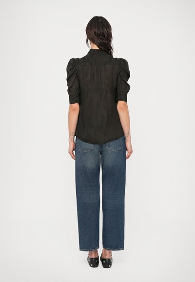 Mustrueritud must pluus lühikeste puhvisvarrukatega, kombineeritud helesiniste laiade teksapükstega. Mõlemal riideesemel on peened tekstuurid.