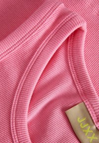 Roza rebrasta tkanina z gladko teksturo, ki ima zložen rob in oznako z "JXXX" v zeleni barvi.