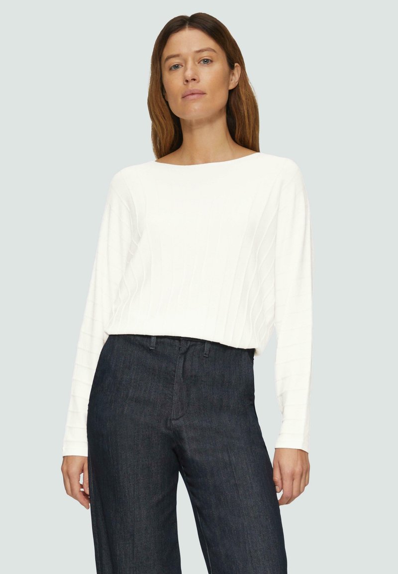 Weißes, geripptes Langarmoberteil, kombiniert mit dunkelblauen, hoch taillierten Jeans. Das Oberteil hat einen Bootsausschnitt und eine lässige Passform.